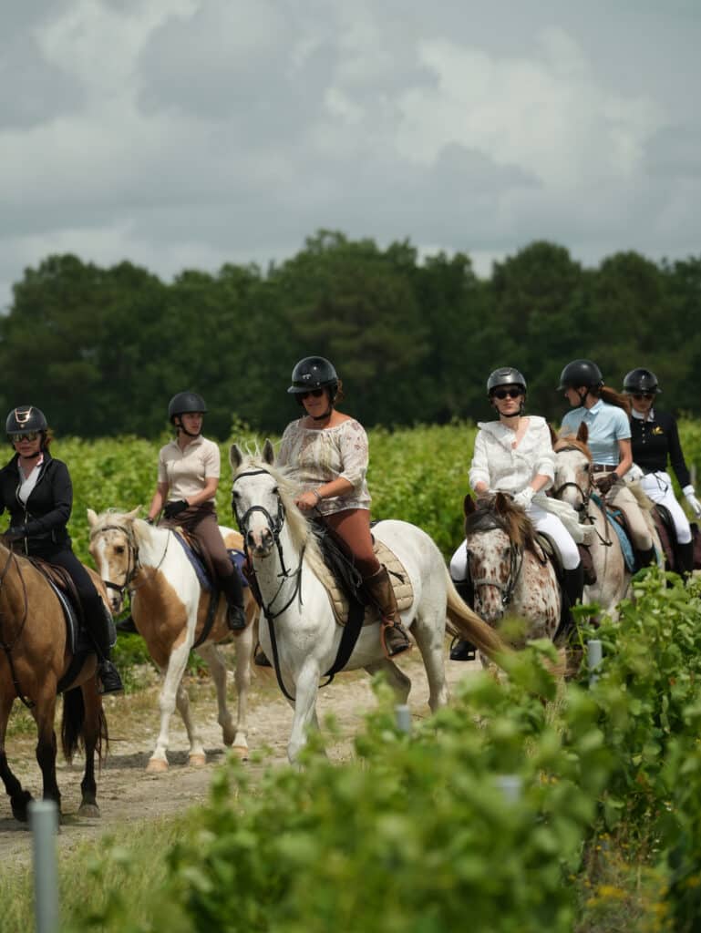 Groupe de femmes en randonnée équestre dans un vignoble sous un ciel nuageux.